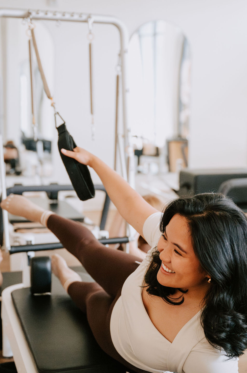 A smiling client using a Reformer with Tower attachment at Packard Row