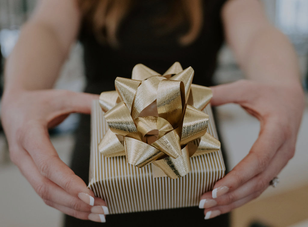 Hands holding a wrapped gift with a gold bow - a Core Collective gift card