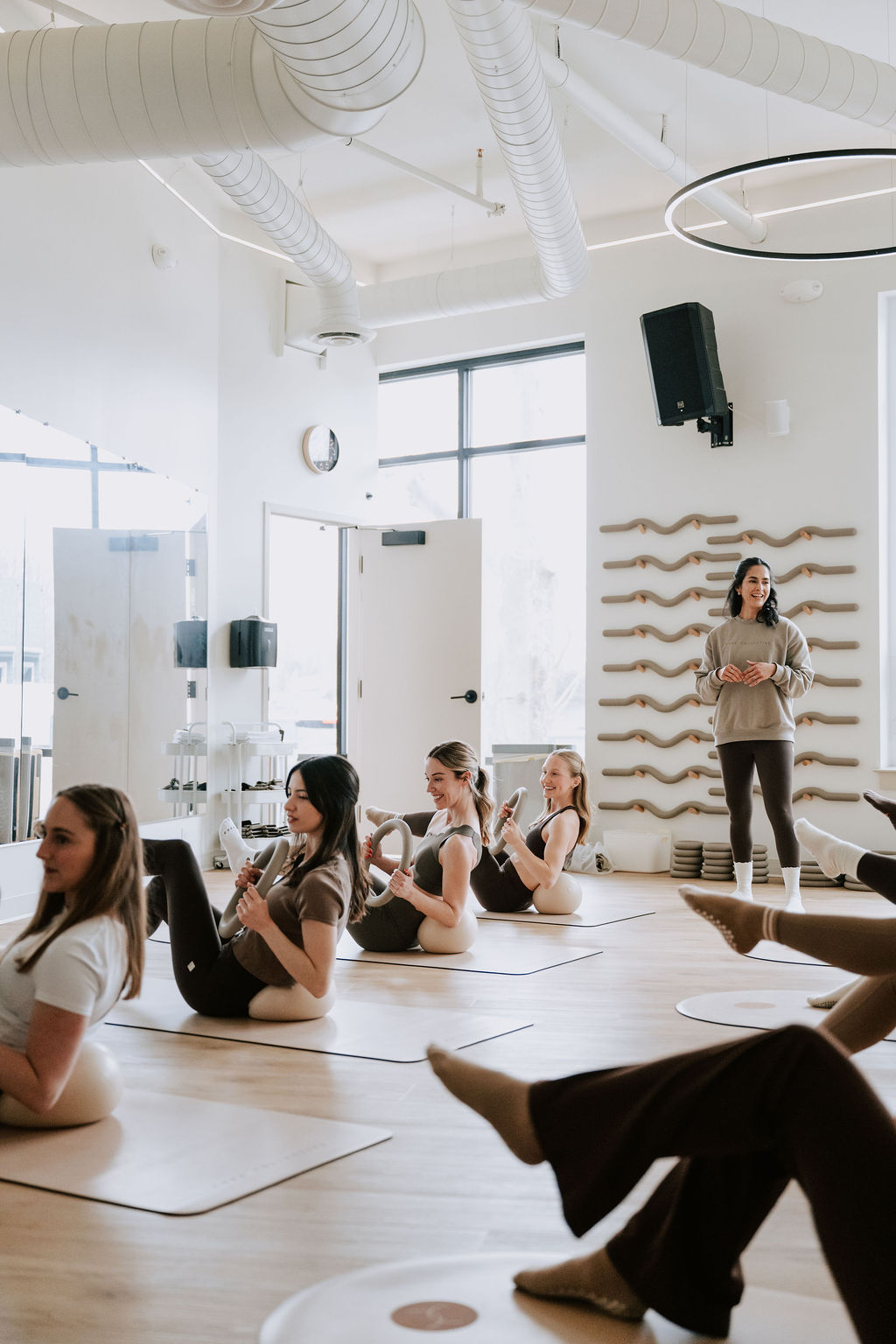 Clients sitting on mats holding Pilates rings while an instructor coaches from the front of the studio