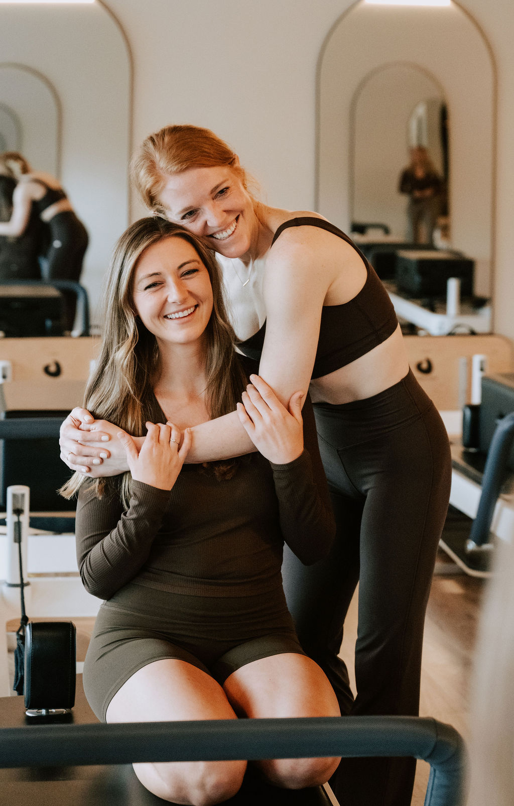 Two Core Collective members hugging and laughing on a reformer